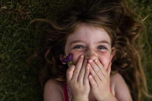 Girl lying on grass outside with flowers - Australian Stock Image