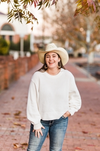 Girl on street laughing with hand in pocket wearing hat - Australian Stock Image