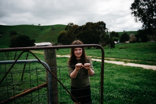 Girl opening a farm gate, looking at camera