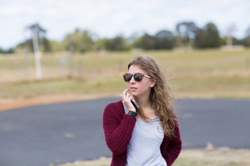 Girl outside wearing sunnies holding mobile phone - Australian Stock Image