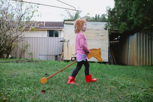Girl playing with a wooden hobby horse in a backyard - Australian Stock Image