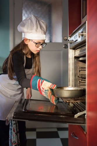 Girl putting cake into oven