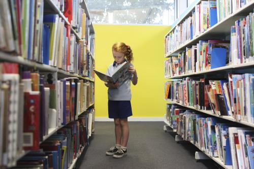 Girl reading a book in a library - Australian Stock Image