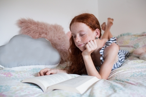 Girl reading a book on a bed - Australian Stock Image