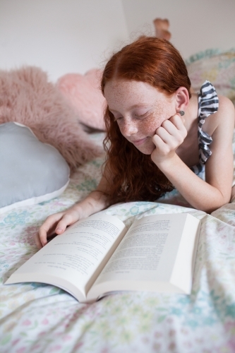 Girl reading a book on a bed - Australian Stock Image