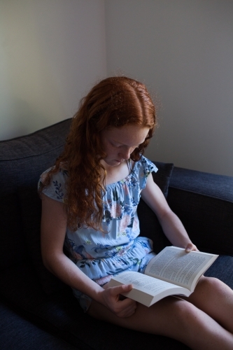 Girl reading a book on a lounge - Australian Stock Image