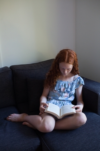 Girl reading a book on a lounge - Australian Stock Image