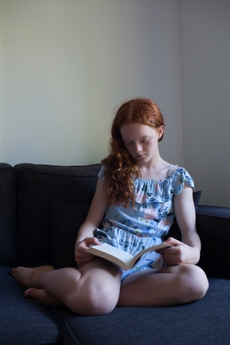 Girl reading a book on a lounge - Australian Stock Image