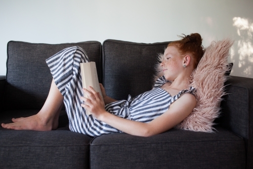 Girl reading a book on a lounge - Australian Stock Image