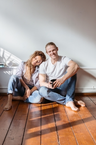 Girl resting her head on the shoulder of a guy while seated on wooden floor - Australian Stock Image