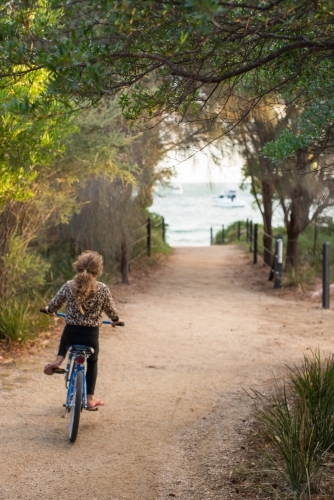 Girl riding a bike on gravel surrounded by trees and beach