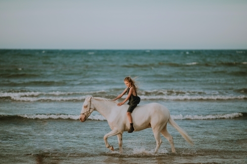 Girl riding horse in ocean waves - Australian Stock Image