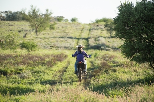 Girl riding motorcycle on grassy farm track - Australian Stock Image