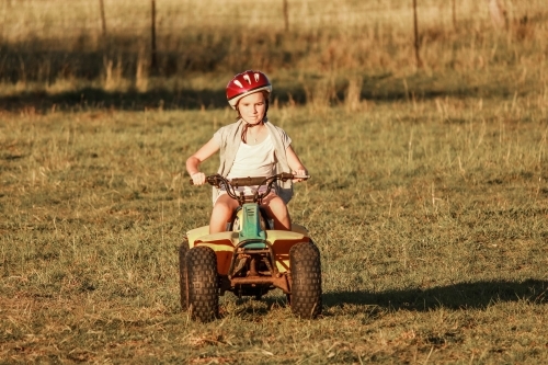 Girl riding quad bike wearing helmet on farm - Australian Stock Image