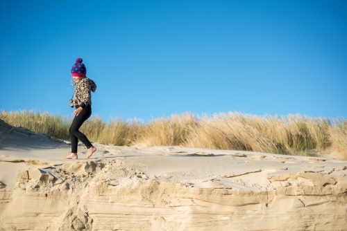 Girl rugged up in jacket and beanie walking on sand dunes in winter - Australian Stock Image