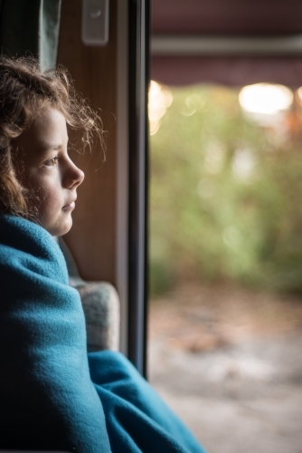 Girl rugged up inside caravan door looking out to bush - Australian Stock Image