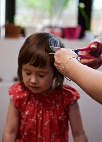 Girl sitting on a chair having her hair cut by her mother - Australian Stock Image