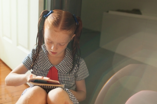 Girl sitting on the floor reading a book - Australian Stock Image