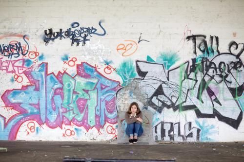 Girl sitting with graffiti on wall