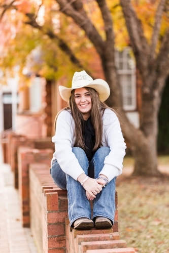 Girl smiling sitting on brick wall - Australian Stock Image