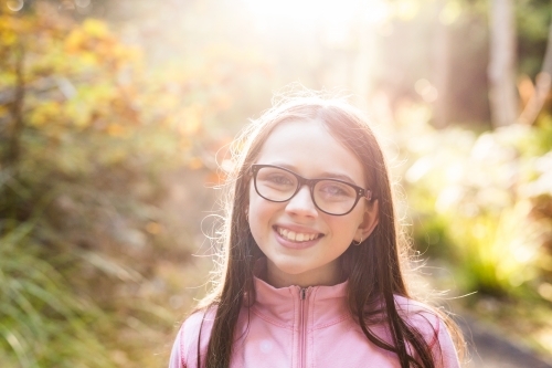 Girl standing in forest backlit by sun - Australian Stock Image