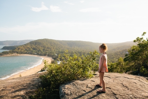 Girl standing on a rock looking at the view over a beach