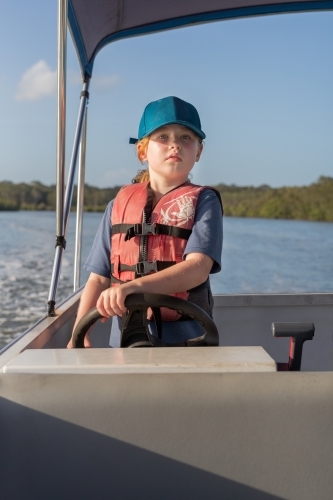 Girl steering a boat wearing a life jacket - Australian Stock Image