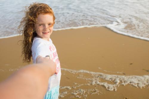 Girl walking along the beach holding hands - Australian Stock Image