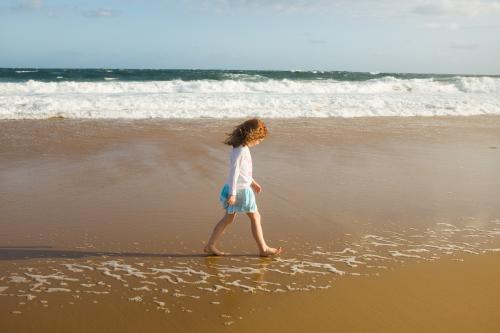 Girl walking along the shoreline at the beach - Australian Stock Image