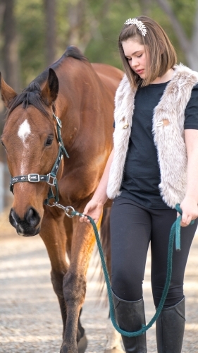 Girl walking horse along dirt track - Australian Stock Image