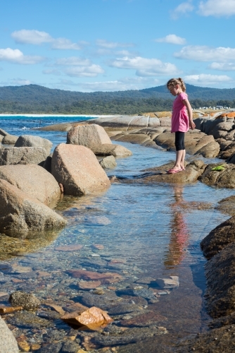 Girl walking over boulder rocks and rockpools at beach
