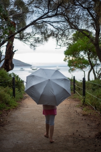 Girl walking to ocean under an umbrella surrounded by trees