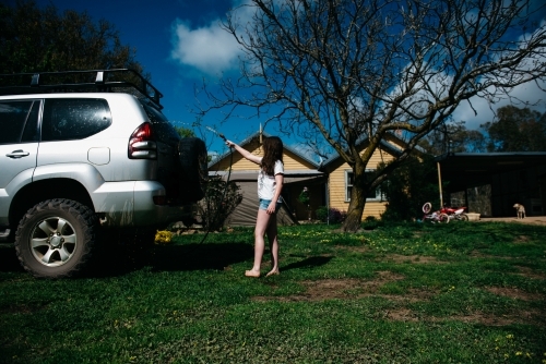 Girl washing car with house in background