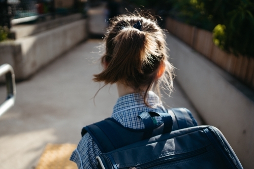 Girl with a ponytail in a school dress with a backpack walks along a path
