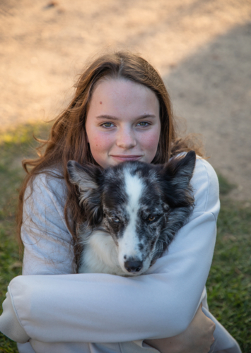 Girl with long hair smiling in portrait and hugging her dog - Australian Stock Image