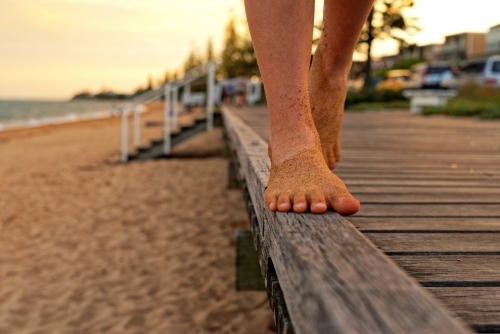 Girl with sandy feet balancing on the edge of a boardwalk as sunset