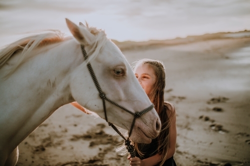 Girl with white horse on the beach at sunset