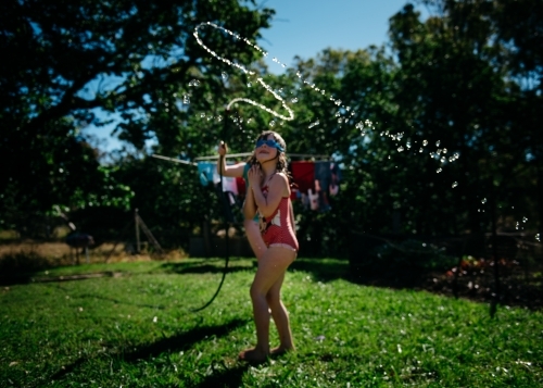 Girls playing under hose, brunette girl looking up, soft focus - Australian Stock Image