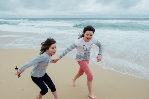 Girls running on the beach holding hands