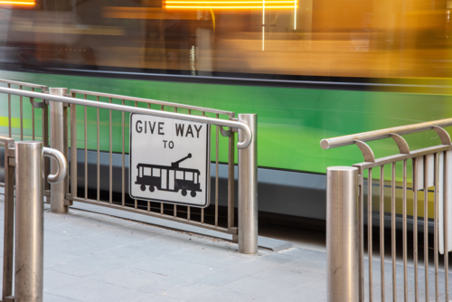 Give way to trams sign at a tram stop with a tram moving past - Australian Stock Image