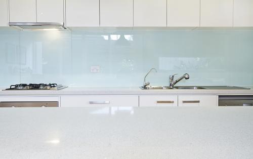 Glass kitchen splashback and white counter tops in designer home - Australian Stock Image