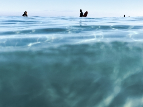 glassy blue oceans with silhouetted surfers sitting on the horizon - Australian Stock Image