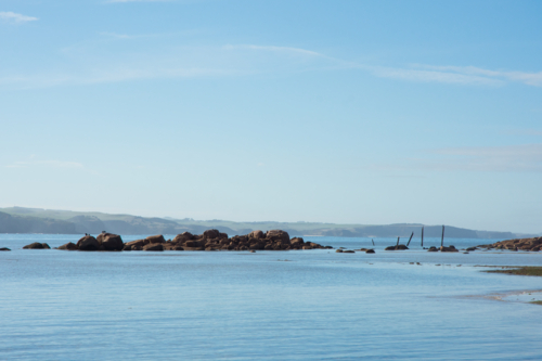 Glassy sea, rocks and old jetty on a sunny day - Australian Stock Image