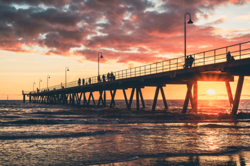 Glenelg Beach jetty with people strolling along at sunset, South Australia - Australian Stock Image