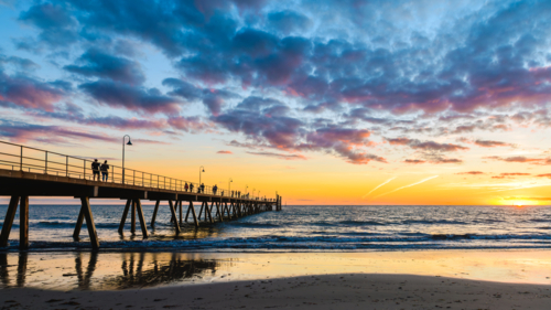 Glenelg Beach pier with walking people silhouettes at sunset at sunset, South Australia - Australian Stock Image
