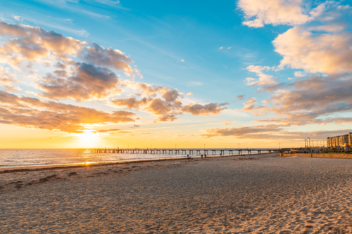 Glenelg Beach with jetty and people walking along the shore during sunset, South Australia - Australian Stock Image