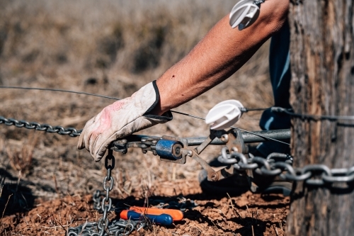 Gloved hand fixing wires of a fence - Australian Stock Image