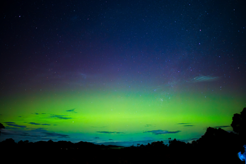 glowing green and blue aurora over dark landscape - Australian Stock Image