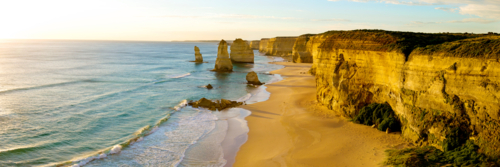 Golden cliffs and sea stacks glow in evening light along a rugged ocean coast. - Australian Stock Image