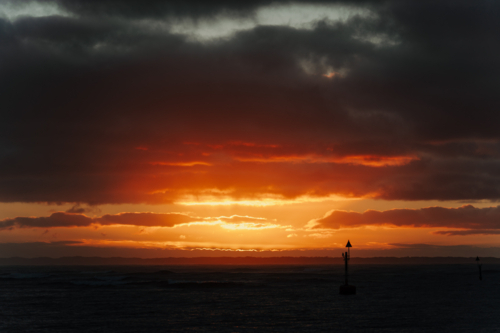 golden coastal sunset partially hidden behind a dense layer of clouds - Australian Stock Image
